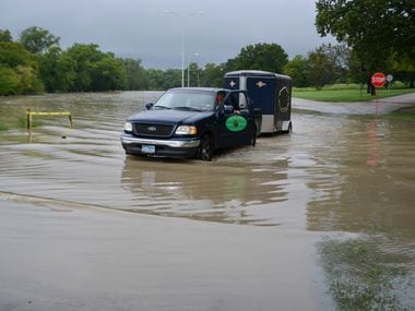 A pickup hauling a trailer drives through waters flooding out of the banks of White Rock...