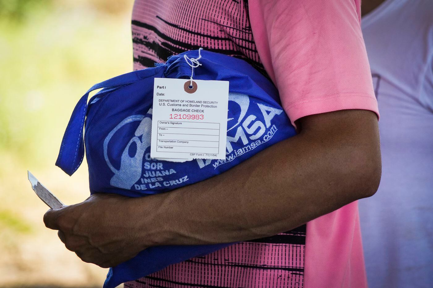 A migrant holds his belongings in a bag tagged with a U.S Customs and Border Protection...