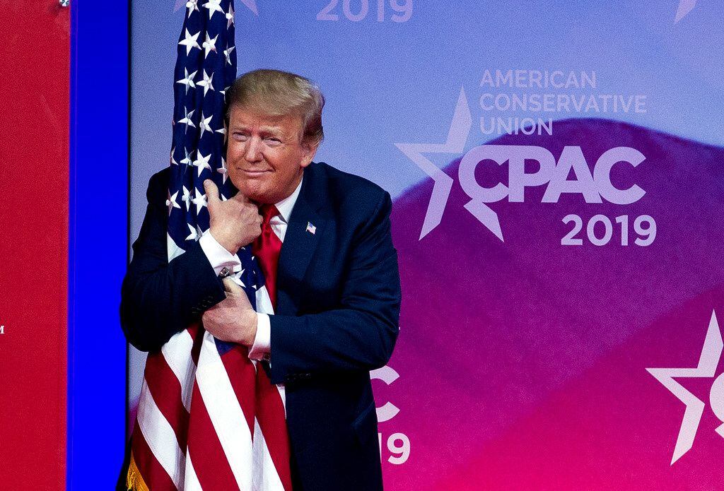President Donald Trump hugs the American flag as he arrives on stage to speak at the Conservative Political Action Conference, CPAC 2019, in Oxon Hill, Md., on March 2, 2019.