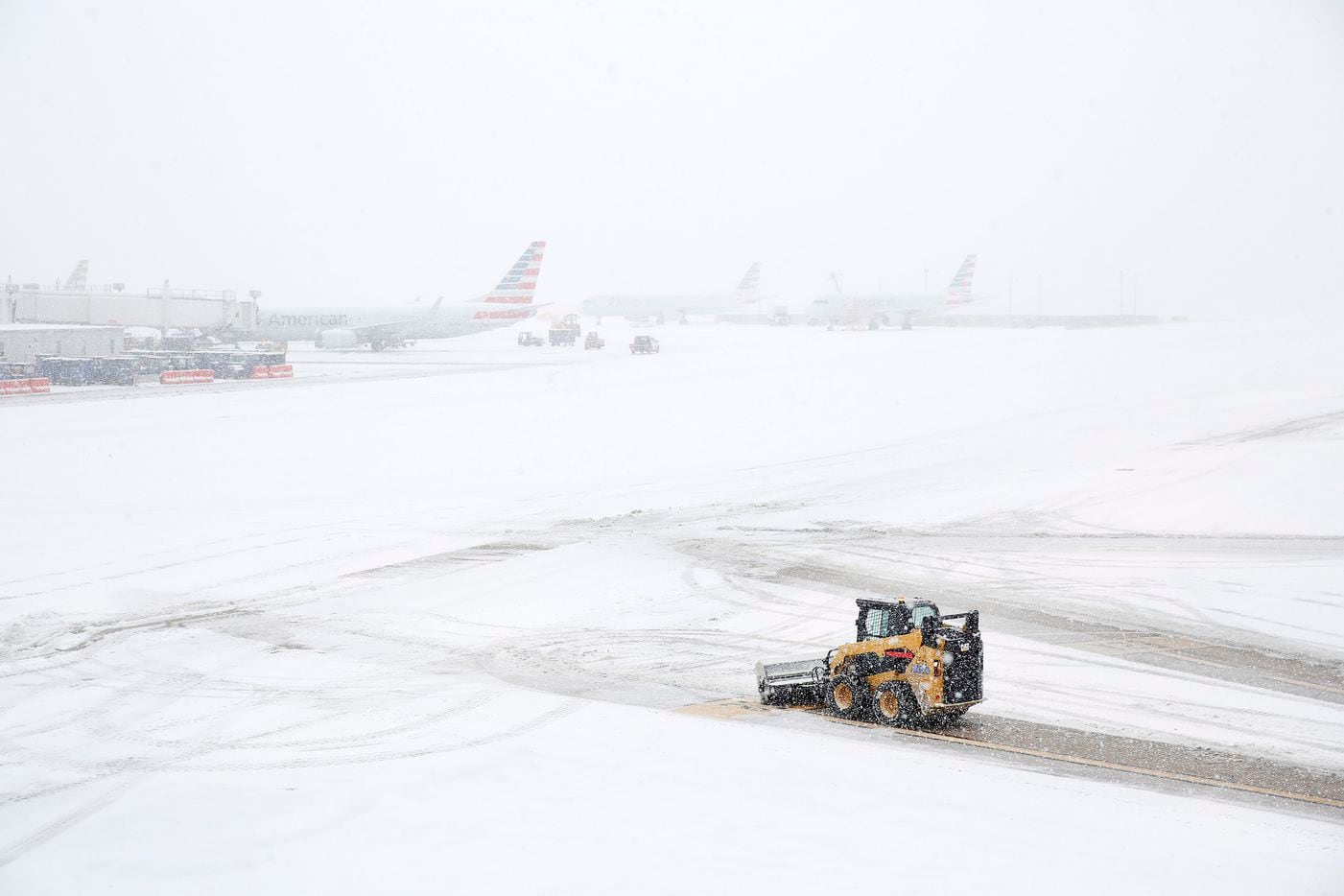 With sleet turning to blowing snow, ground crews clear gate guidance markings at DFW...