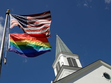 A gay pride rainbow flag flies along with the U.S. flag in front of a United Methodist...