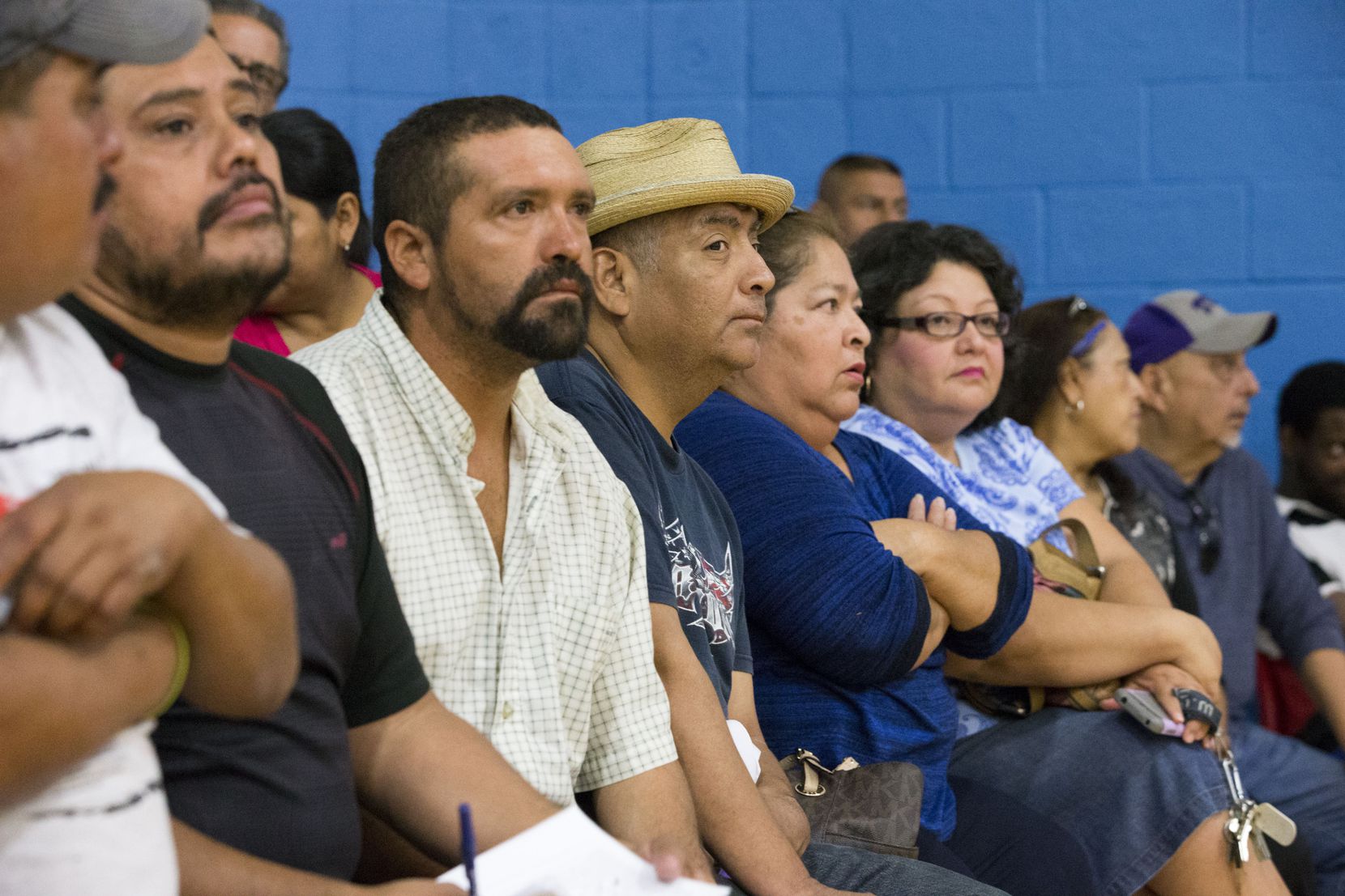 Community members listen to announcements during a community meeting regarding upcoming mass...