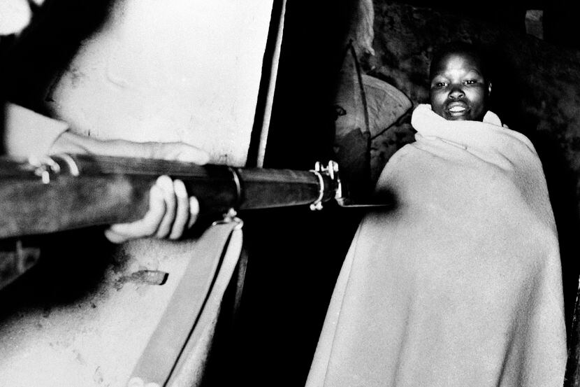 A member of the Mau Mau, wrapped in the blanket in which he was sleeping, is held at gun...