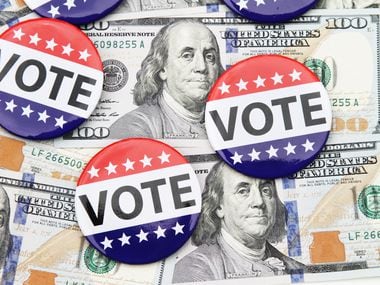 VOTE campaign buttons on top of scattered hundred dollar bills spread out beneath it. Concept image illustrating election funding, political donations, Super Pac money, political bribes.