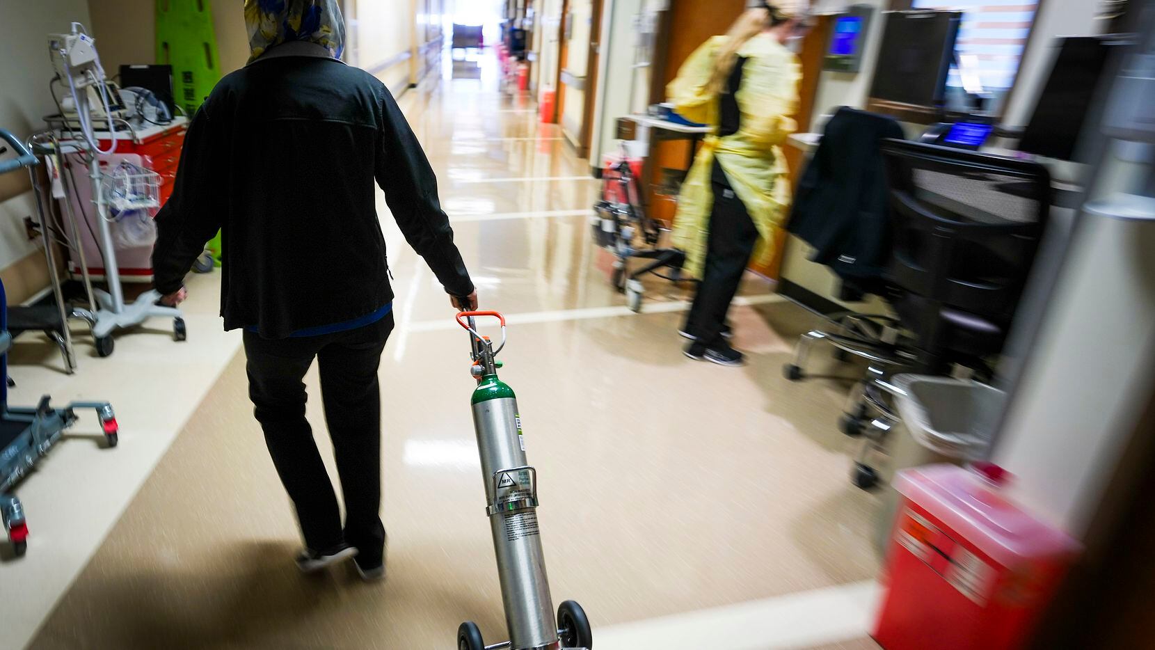 Fara Ajani, associate manager in medicine services, pulls an oxygen cylinder down a hallway...