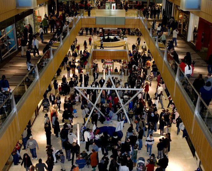 Mall goers make their way around the 15-foot brushed metal Hanukah Menorah at the Dallas...