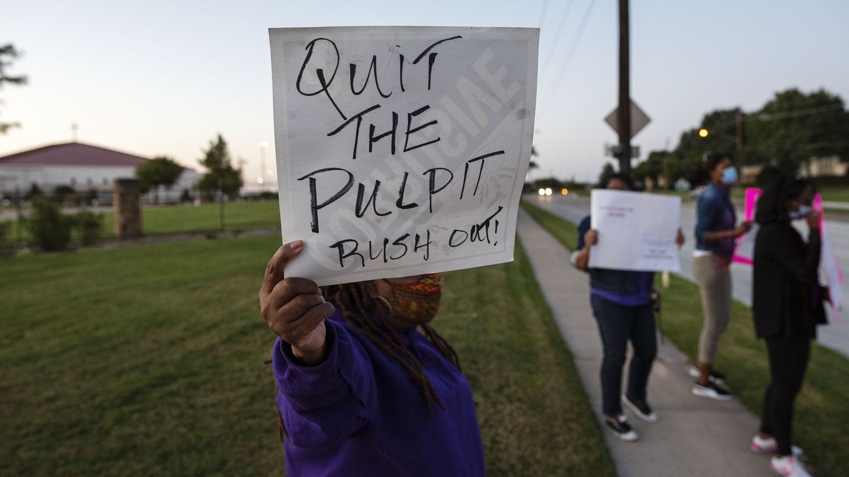 Women's advocate Diane White, center, holds a sign calling for Rickie Rush to step down as Pastor of The Inspiring Body of Christ Church in Dallas.  She and other advocates demonstrated outside the church Monday evening.