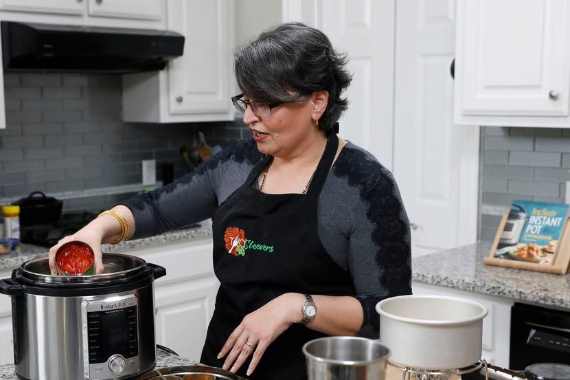 Urvashi Pitre of Keller, Texas prepares butter chicken by adding a can of tomatoes in an...