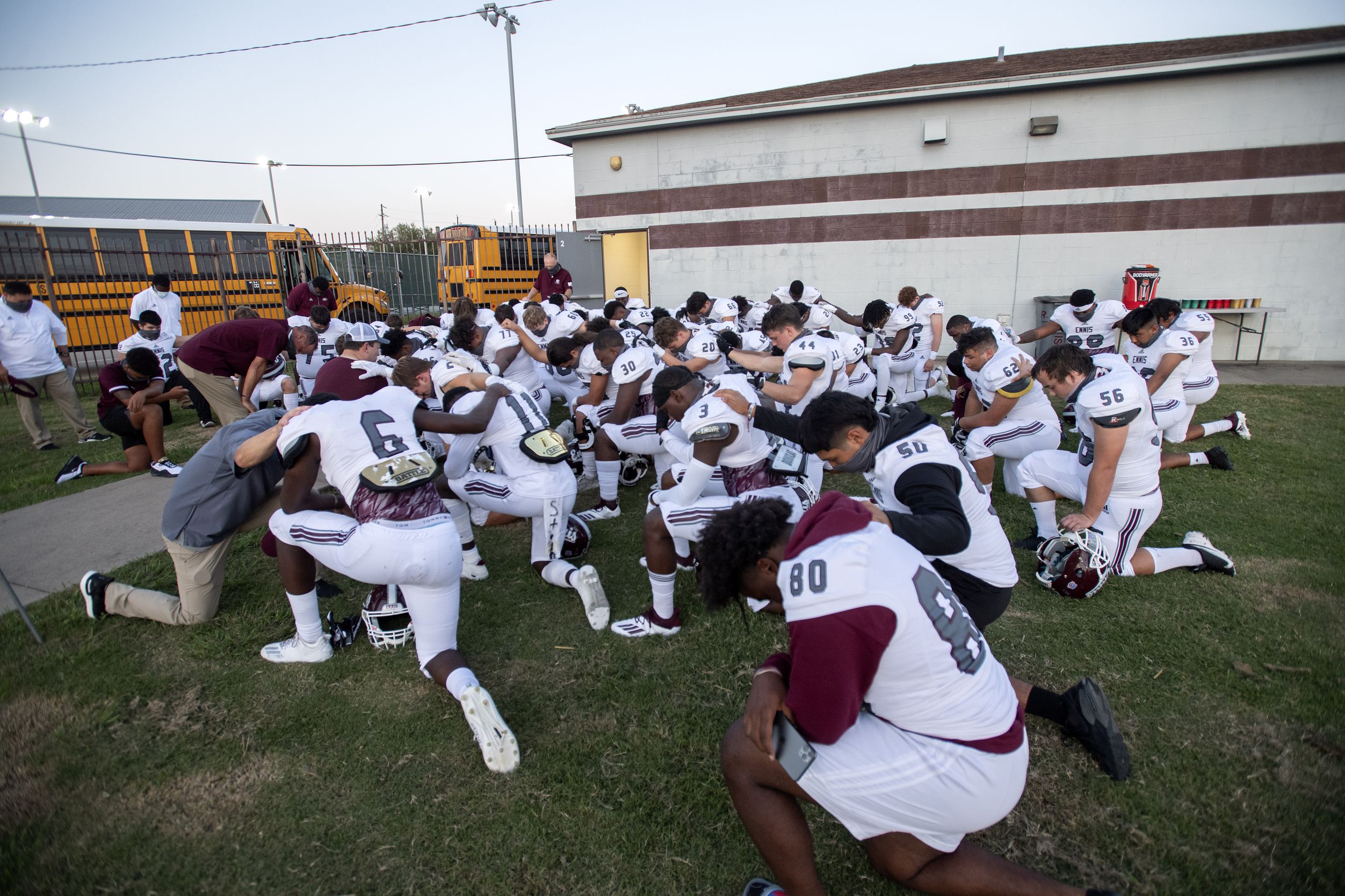 Ennis players and coaches pray before a high school football game against Red Oak on Friday,...