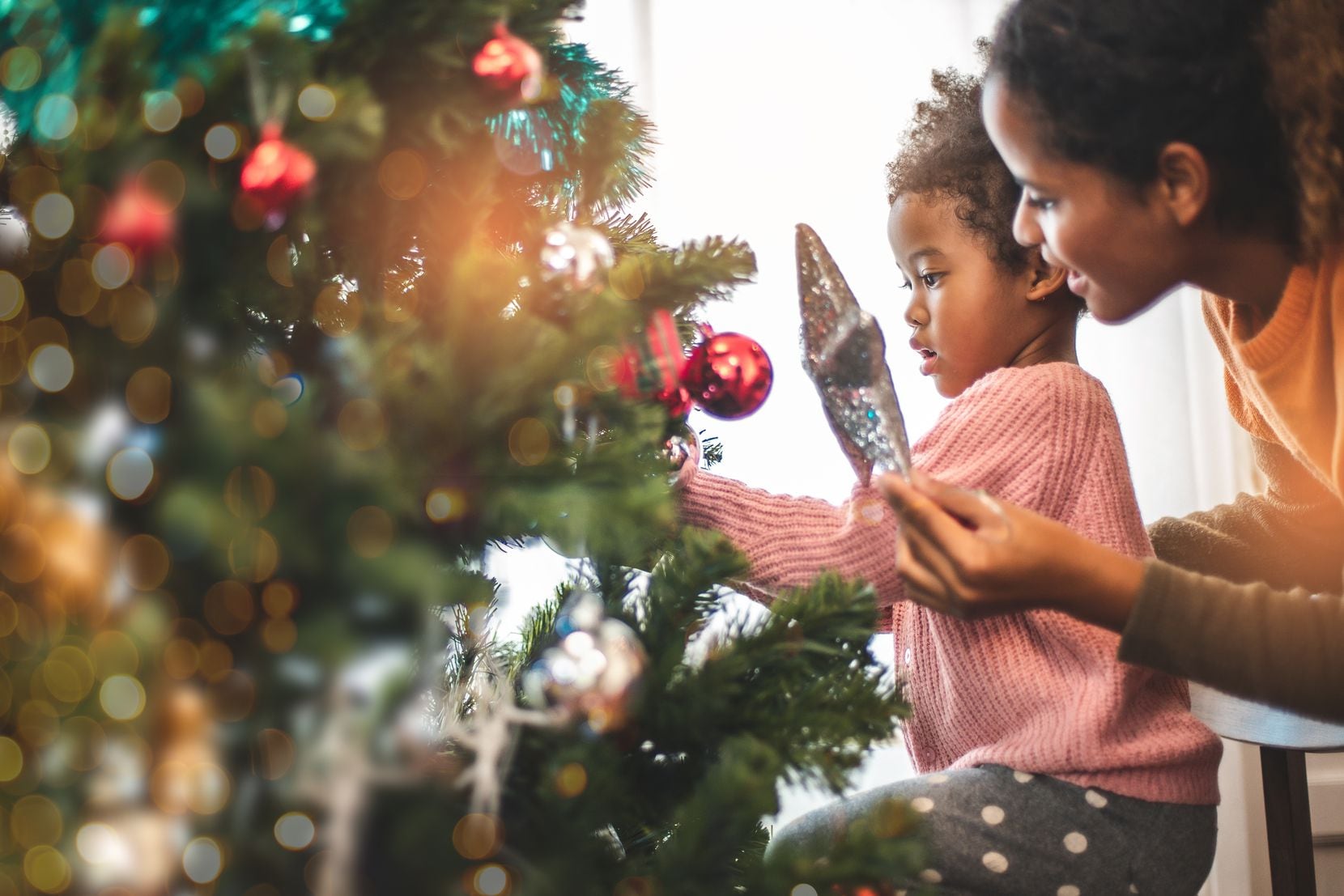 A parent and daughter decorate the Christmas tree the morning before Christmas.