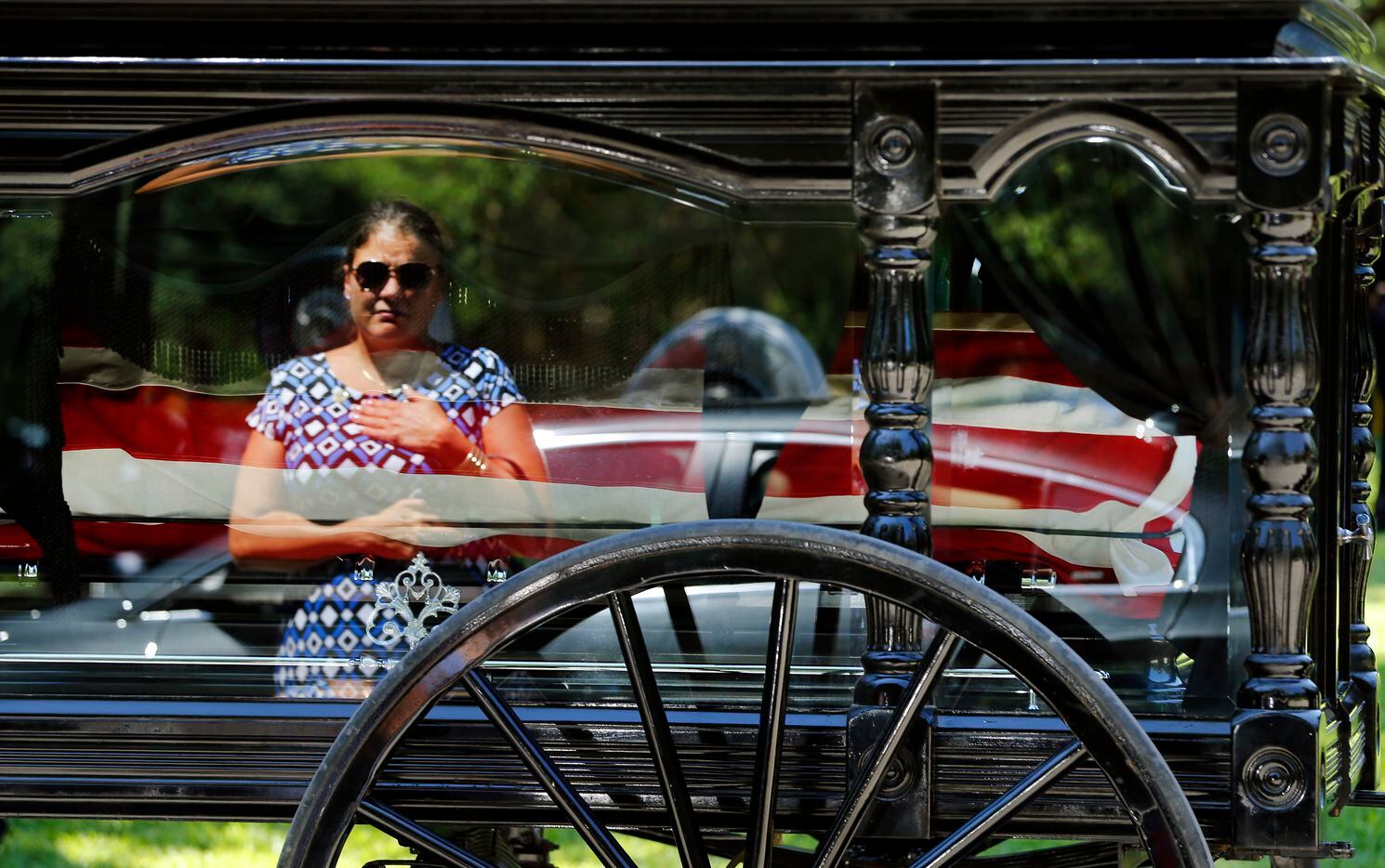 In the reflection of the horse-drawn caisson, a Smith family member places her hand over her...