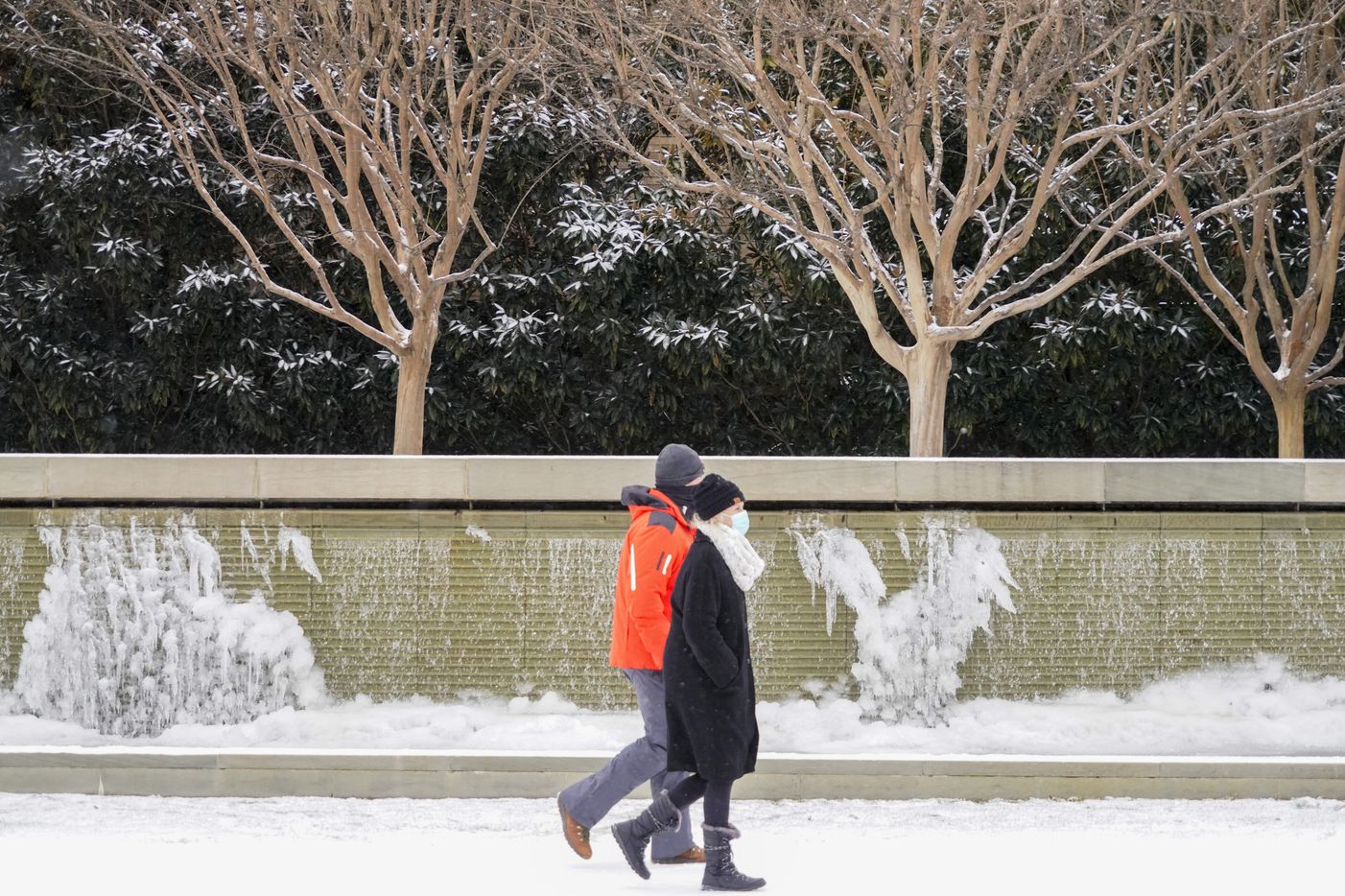 People walk past frozen fountains on Hillcrest near Lovers lane as a winter storm brings...