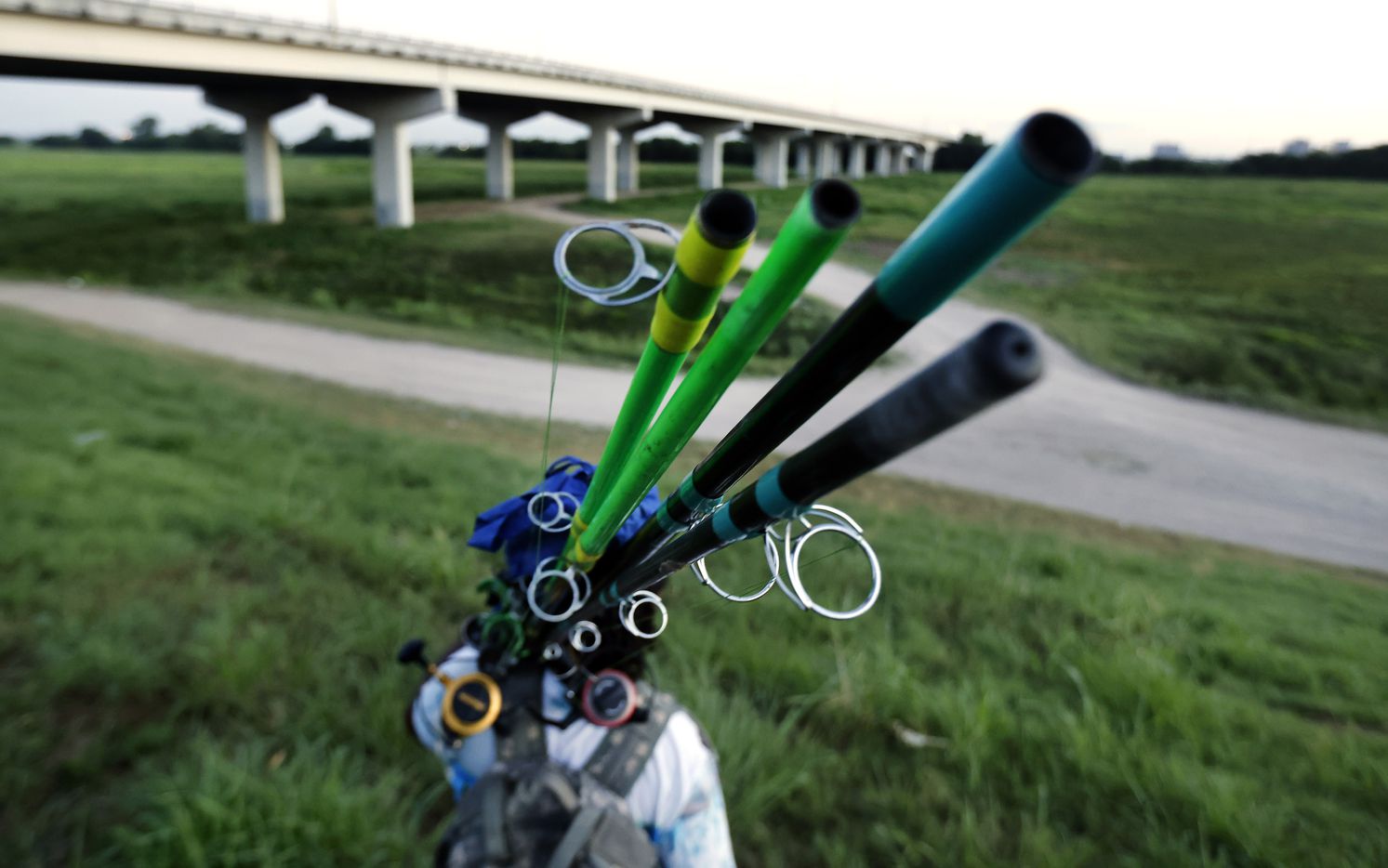 Odell Allen carries a pair of segmented 12 ft fishing poles he uses to fish for alligator gar on the Trinity River near the Westmoreland bridge, Monday, August 30, 2021.  (Tom Fox/The Dallas Morning News)