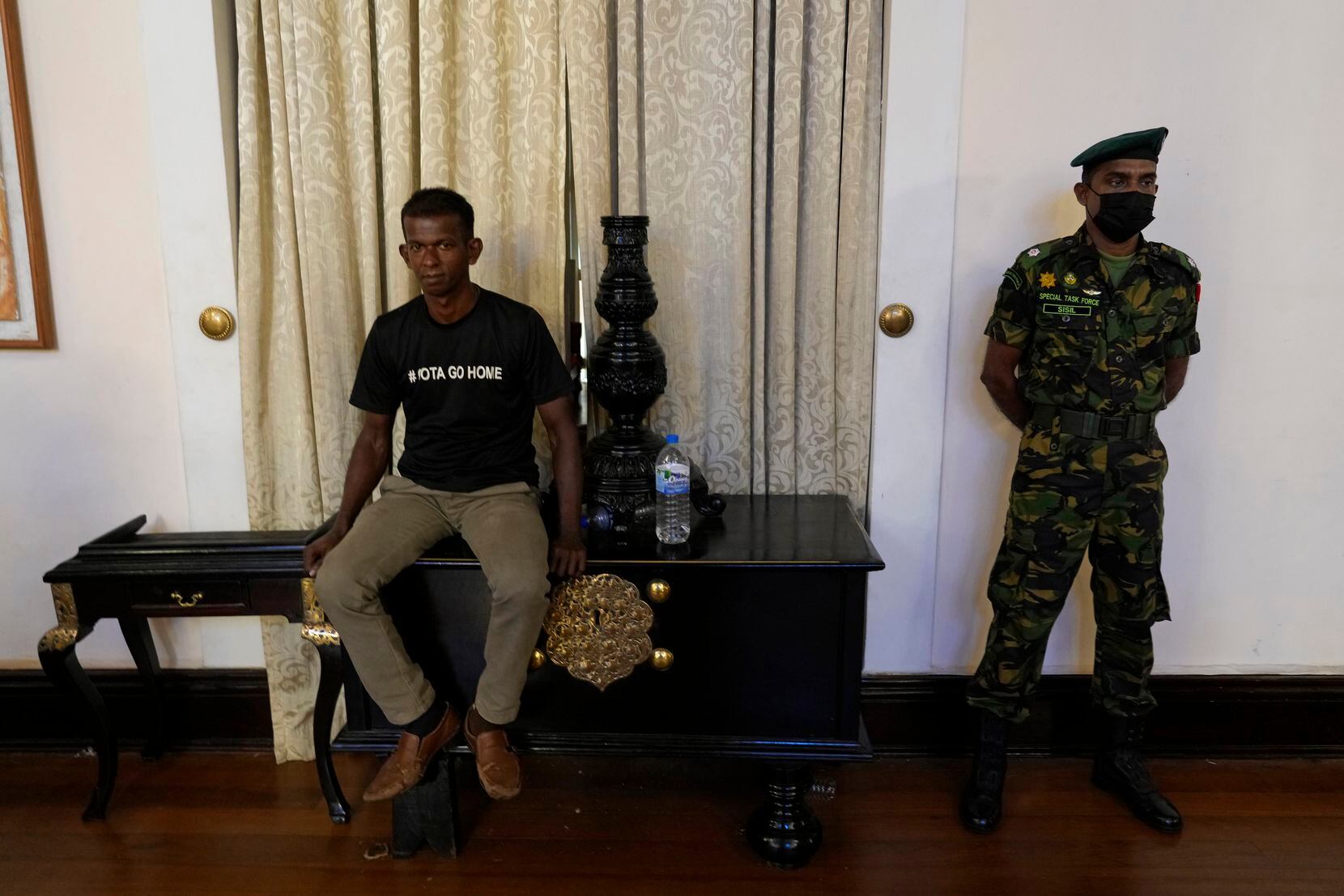 Sri Lanka army officer stands guard as a protester sits on the table inside the official...