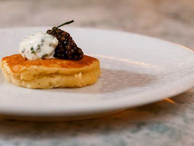 A Buckwheat Potato Blini topped with Osetra Caviar and Chive Crème fraîche sits plated at...