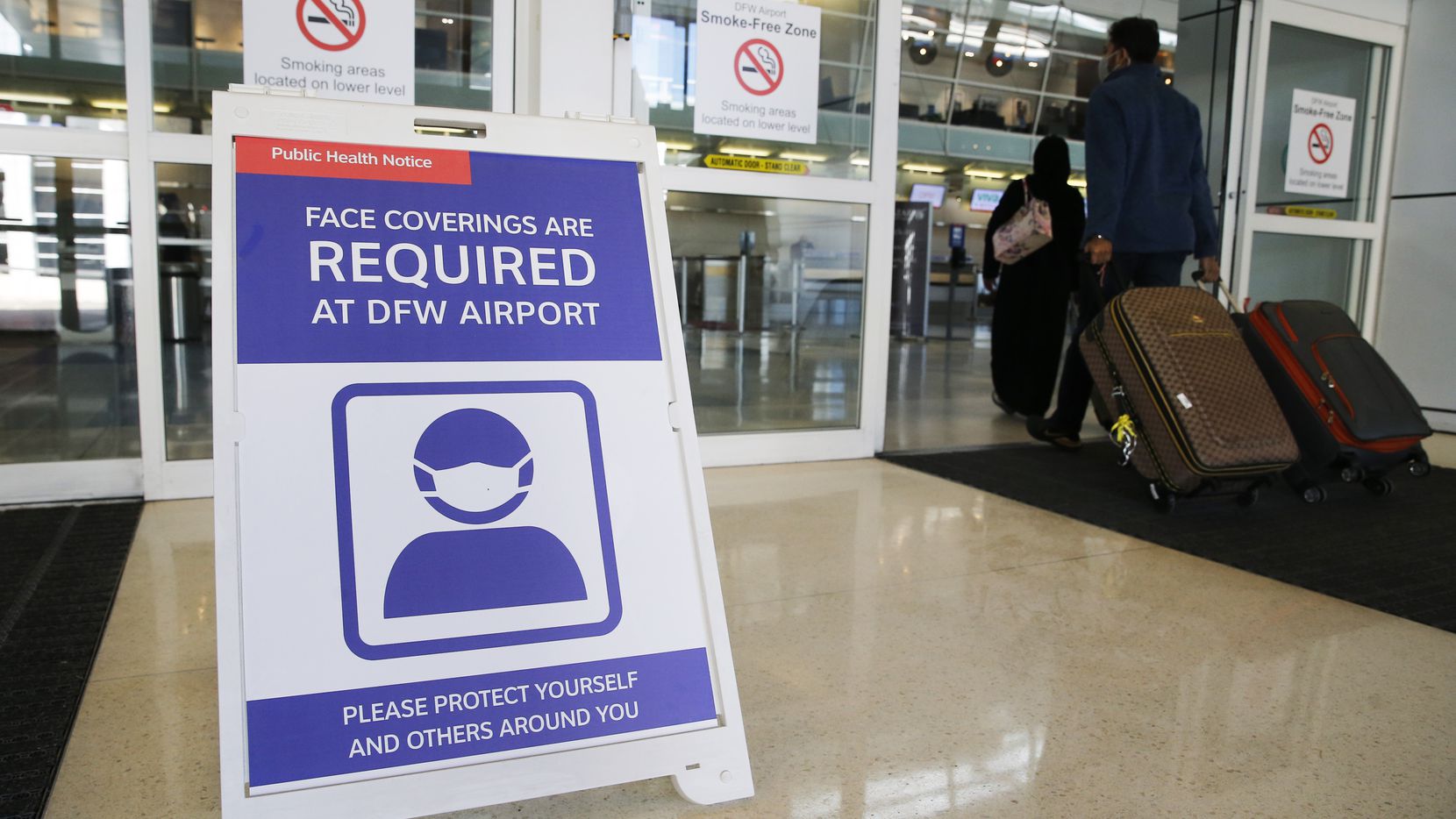 A sign notifying travelers to wear a mask as people make their way into Terminal D at DFW International Airport on Monday, November 16, 2020. (Vernon Bryant/The Dallas Morning News)