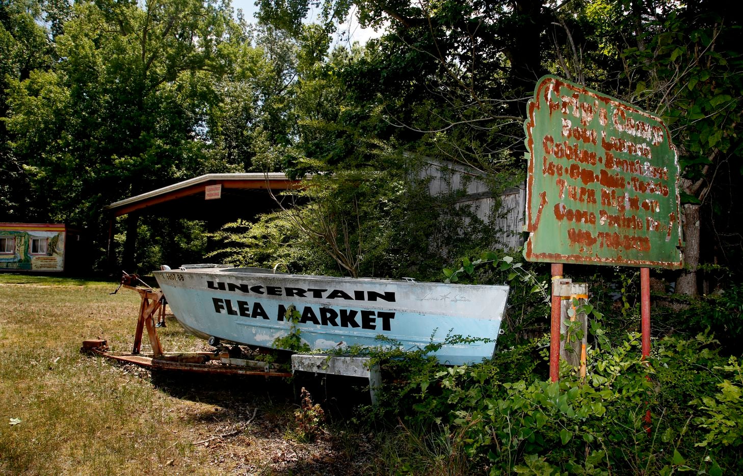A faded sign advertising Crip's Camp stands beside an old boat advertising a flea market...