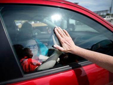 Volunteer Karen Kirk of Houston gives a student a high-five through the window after they made their drive-thru meal pickup outside AT&T Stadium in Arlington, Texas, Saturday, March 28, 2020. Arlington Charities, Fielder Road Baptist Church and Tarrant Area Food Bank volunteers loaded school parents vehicles with weekend meals for Arlington ISD families. After last week's drive-thru pick up, organizers moved the operation to the stadium parking lot to accommodate 1,000 pre-registered meals. The line snaked through the parking lot as volunteers worked tirelessly to fill trunks while maintaining social distancing.