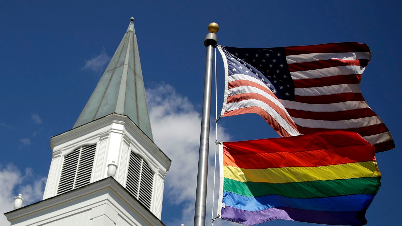 A gay Pride rainbow flag flies with the U.S. flag in front of the Asbury United Methodist...