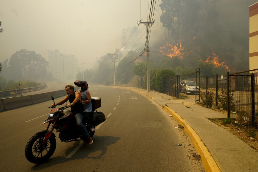 ARCHIVO - Residentes evacúan en una motocicleta entre incendios forestales en Viña del Mar,...