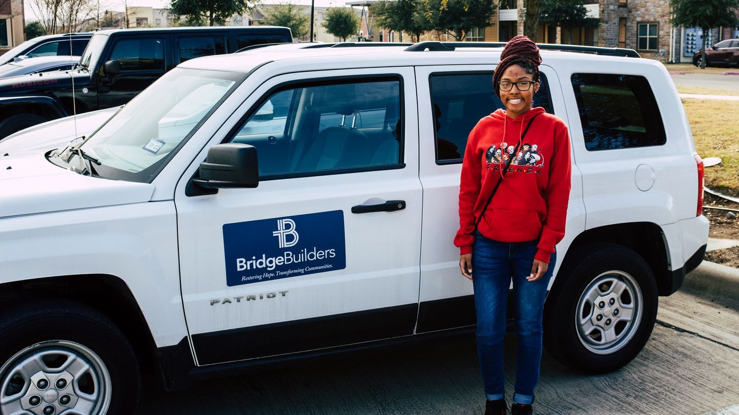 Teen stands next to white SUV with a BridgeBuilders label on it.