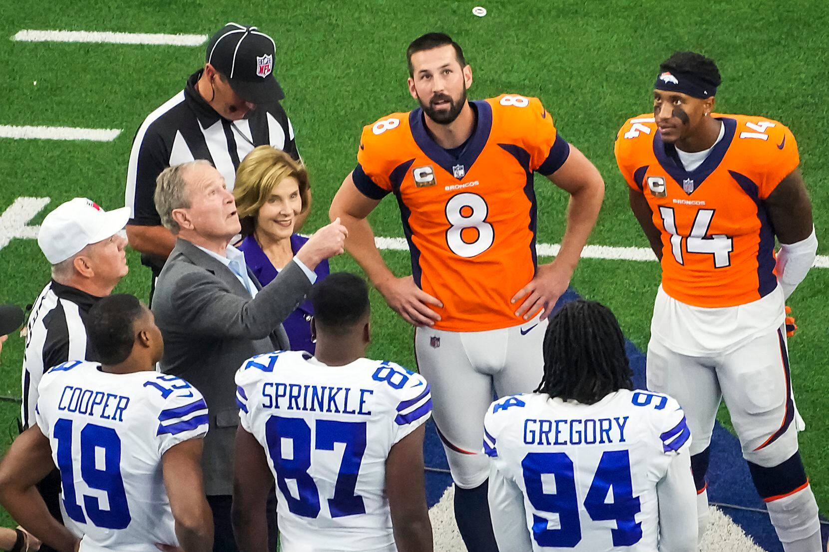 Former President George W. Bush performs the opening coin toss as Laura Bush looks on with Denver Broncos kicker Brandon McManus (8) and wide receiver Courtland Sutton (14) and Dallas Cowboys wide receiver Amari Cooper (19), tight end Jeremy Sprinkle (87) and defensive end Randy Gregory (94) before an NFL football game at AT&T Stadium on Sunday, Nov. 7, 2021, in Arlington. 