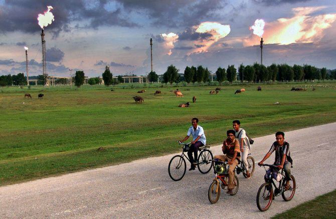 Indonesian men cycle past the enormous Arun natural gas fields in the Aceh, Indonesia.