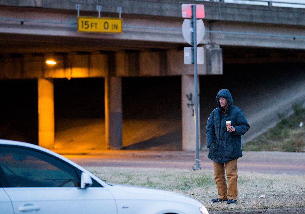 A panhandler holds out a cup to ask for money from drivers on at the corner of Interstate 30...