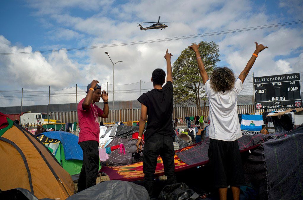 Migrants wave at U.S. border control helicopters flying near the Benito Juarez Sports Center...