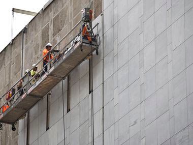 Construction workers use a scaffold to be lifted high above the ground to install marble on...