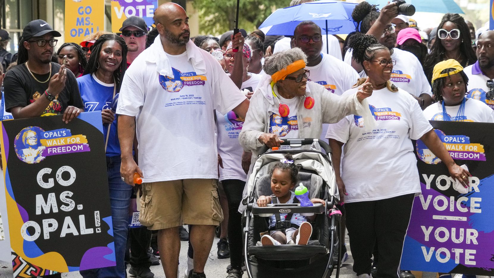 Opal Lee pushes one of her great-granddaughters in a stroller as she waves to musicians...