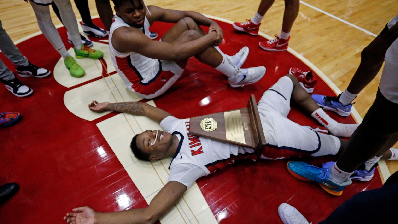 Kimball's Trae Clayton (10) lays spread out on the hardwood, with the championship trophy on...