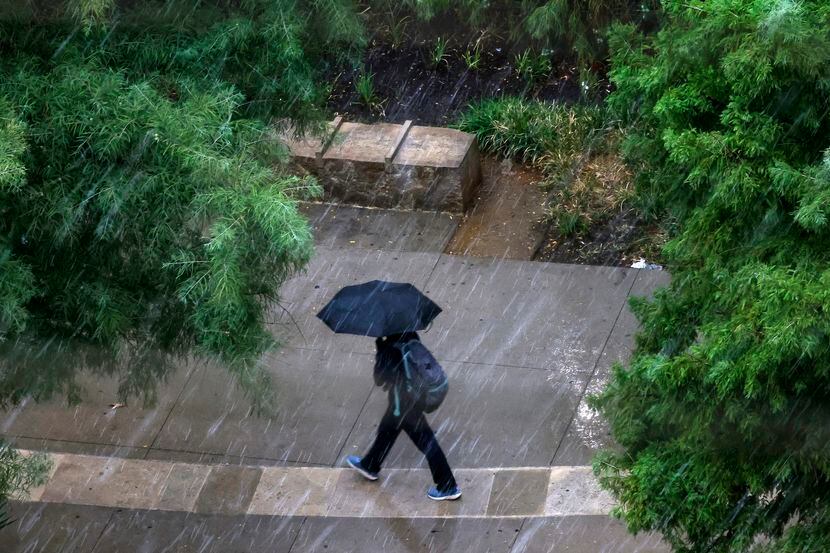 A person takes cover with an umbrella as they hurry through a downpour from the DART train...