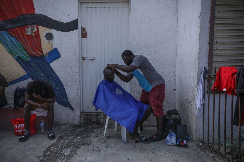 Un hombre corta el cabello a otra persona en un centro de refugio para migrantes en...