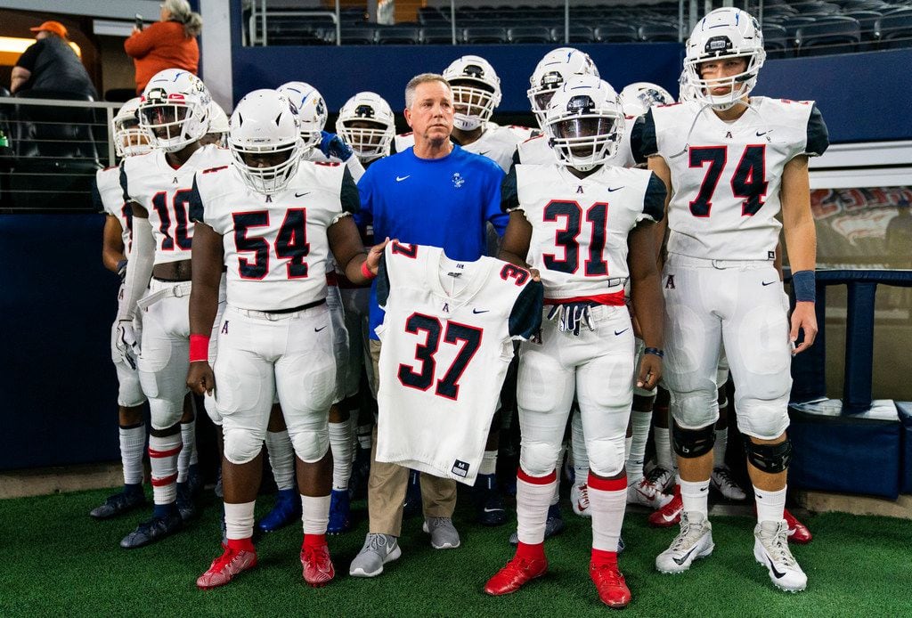 Allen football players and head coach Terry Gambill hold the jersey of Marquel Ellis Jr., a sophomore football player who was shot and killed at a party last week, as they enter the stadium before a Class 6A Division I area-round high school football playoff game between Allen and Rockwall on Friday, November 22, 2019 at AT&T Stadium in Arlington. (Ashley Landis/The Dallas Morning News)
