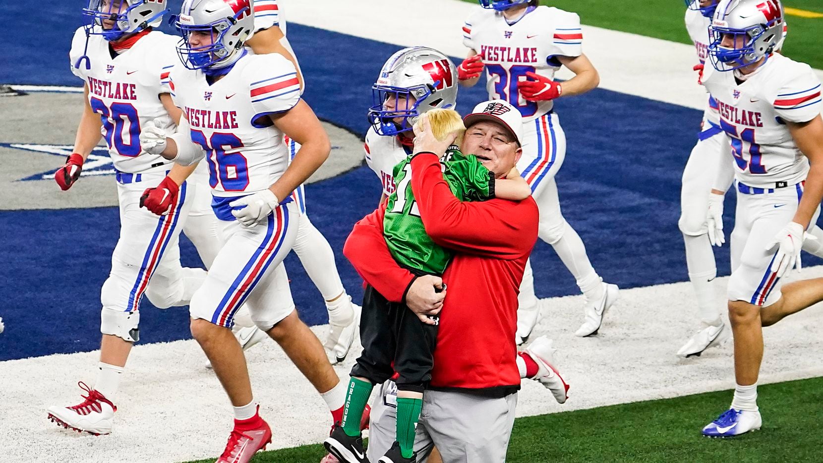 Austin Westlake head coach Todd Dodge hugs his grandson Tate, 5, as his team takes the field to warm warm up before facing his son, Southlake Carroll head coach Riley Dodge, in the Class 6A Division I state football championship game at AT&T Stadium on Saturday, Jan. 16, 2021, in Arlington, Texas.