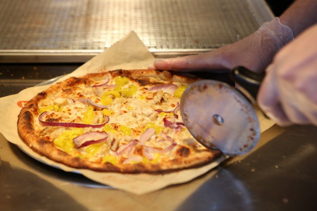 A pizza is sliced after being cooked in a hot, open-flame oven at Blaze Pizza in Frisco.