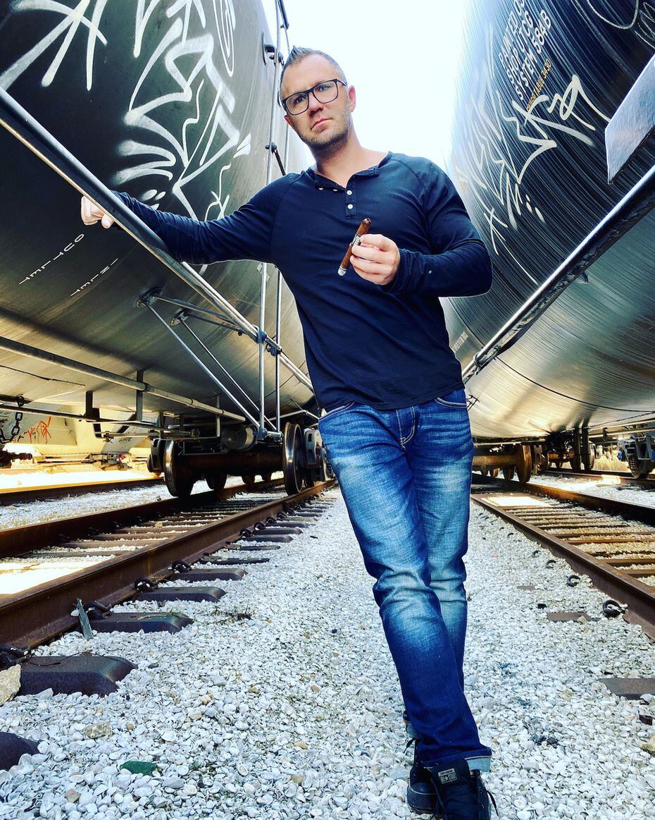Renegade Cigars owner Brandon Hayes poses with a cigar standing on train tracks.