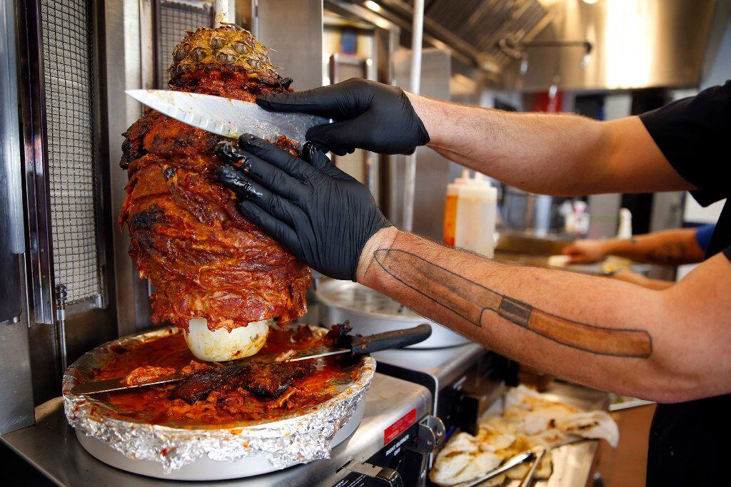 Al Pastor style pork marinated in dried chiles, pineapple juice and spices is shaved off a...