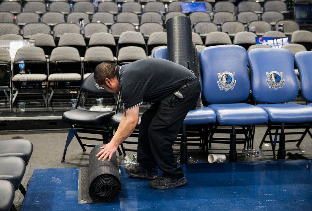 A worker rolls up a carpet in front of the Mavs bench after the Dallas Mavericks beat the...