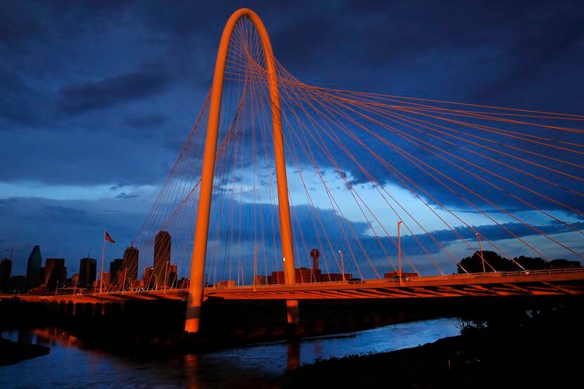 The setting sun illuminates the Margaret Hunt Hill Bridge and downtown Dallas after...