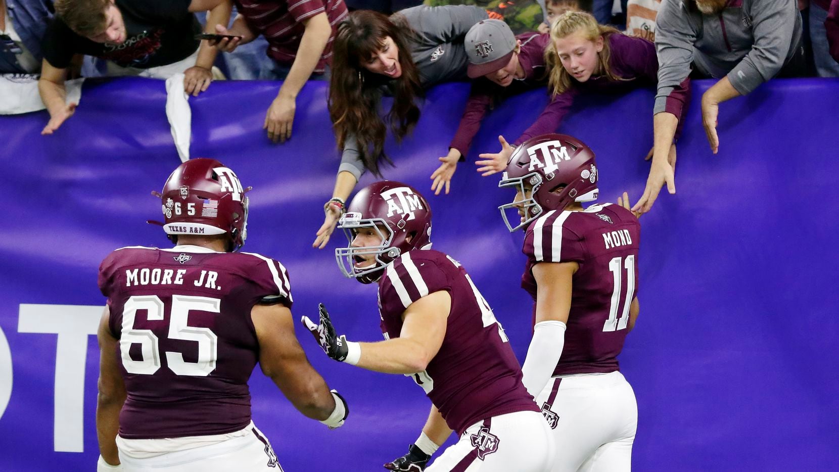 Texas A&M offensive lineman Dan Moore Jr. (65) and tight end Ryan Renick, middle, celebrate as quarterback Kellen Mond (11) high-five fans in the stands after Mond's touchdown during the second half of the Texas Bowl NCAA college football game against Oklahoma State on Friday, Dec. 27, 2019, in Houston.