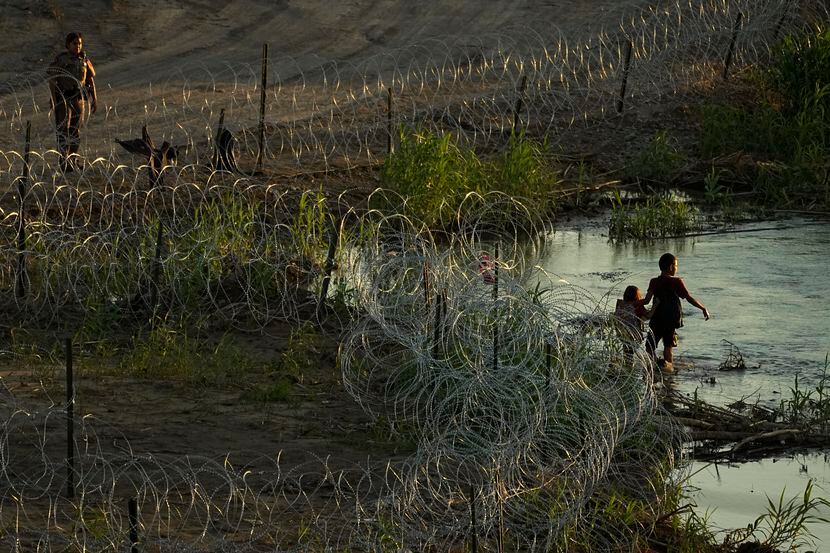 Migrants walk along concertina wire as they try to cross the Rio Grande at the Texas-U.S....