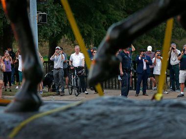 People watch the Robert E. Lee statue being carried on a truck at Robert E. Lee Park in...