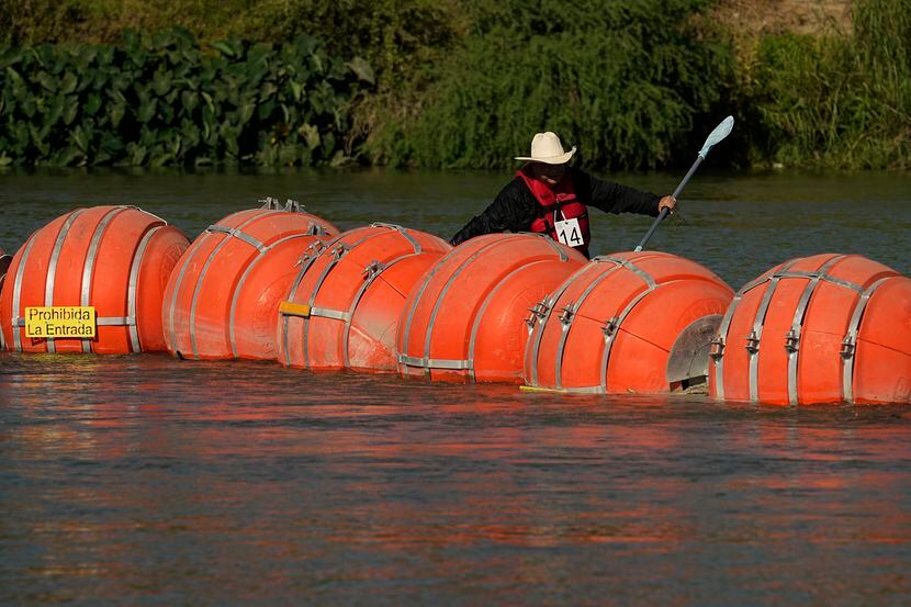A kayaker passes large buoys being used as a floating border barrier on the Rio Grande...