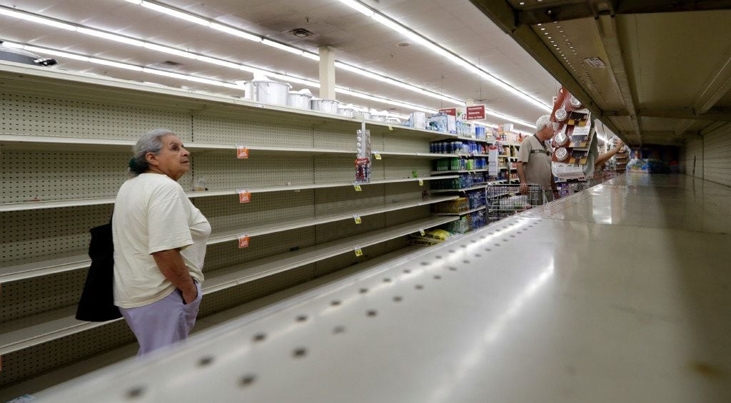 Shoppers pass empty shelves along the bottled water aisle in a Houston grocery store as...