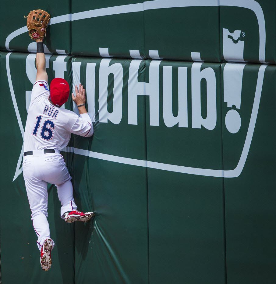 Texas Rangers left fielder Ryan Rua leaps against the outfield wall trying to get to a home...
