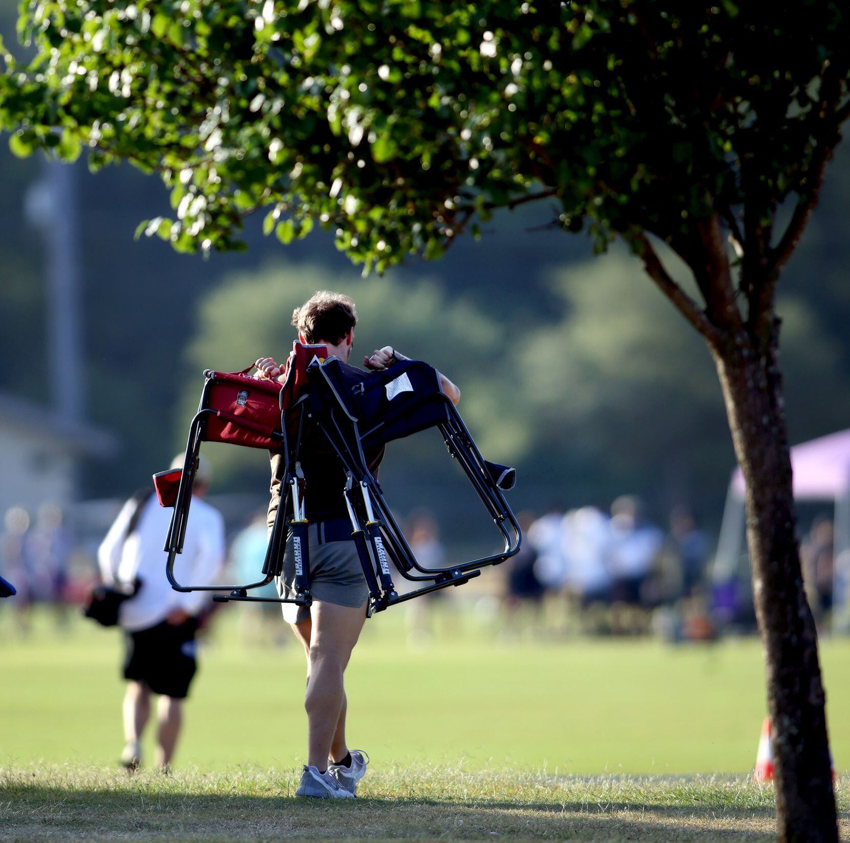 A football enthusiast carries canopy chairs toward one of the playing fields prior to the...