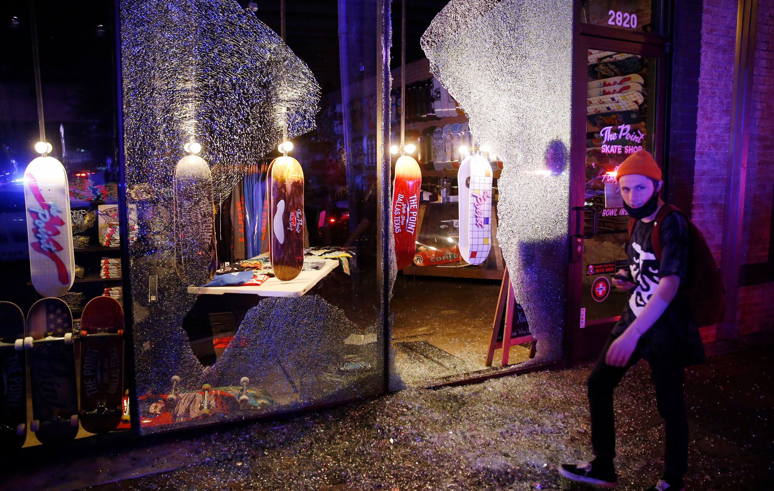People walk by the busted window of The Point Skate Shop along Main Street in Deep Ellum in...