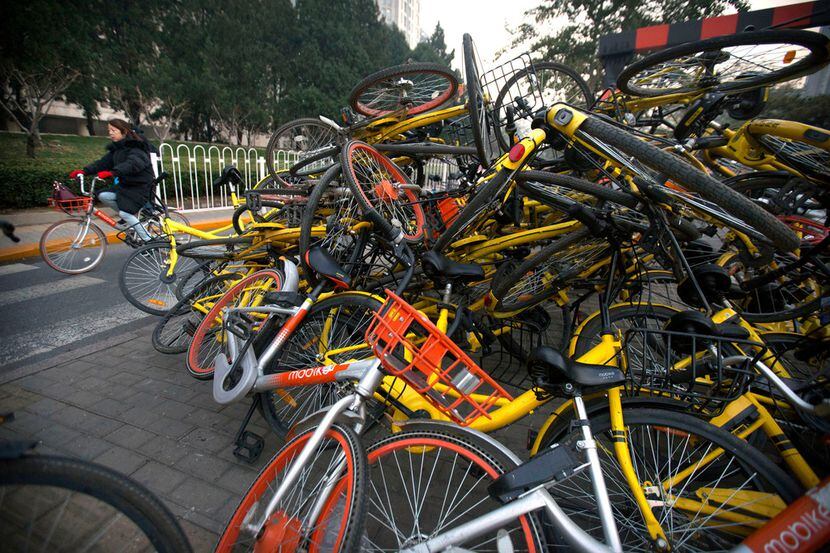 A woman rides a bicycle past Mobike and Ofo branded  bicycles piled on a traffic median in...